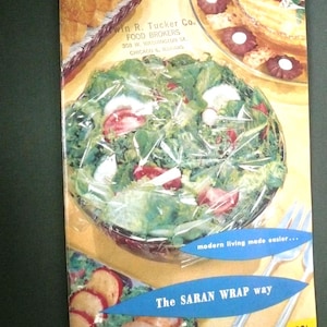 May include: Vintage advertisement featuring a salad bowl wrapped in plastic wrap. The image showcases various food items, including bread, cookies, and sliced fruit. Text includes "Win R. Tucker Co." and "The SARAN WRAP way".