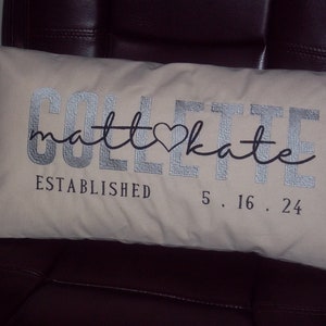 May include: Cream-colored rectangular pillow with silver embroidered text. The pillow features the names "COLLETTE" and "matt♡kate" in a script font, along with "ESTABLISHED 5.16.24". A decorative accent for a home.