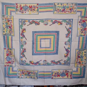 May include: A white tablecloth with a colorful Mexican-themed design. The border features blue, green, yellow, and red stripes and rectangular panels with figures. The center has a square design with similar colors and imagery, including guitars and sombreros.