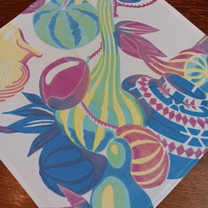 May include: A white fabric kitchen towel with a colorful pattern of gourds, watermelon, and other fruits. The pattern is in shades of blue, green, yellow, pink, and purple.