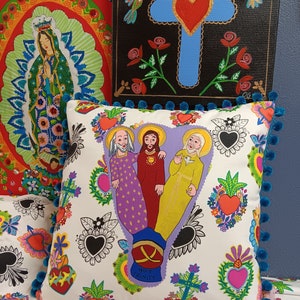 May include: White pillow with a blue trim and pom-poms. The pillow features a colorful illustration of the Holy Trinity with the words "Holy Trinity" at the bottom. The background is filled with hearts, flowers, and other decorative elements.