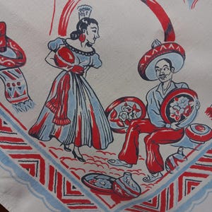 May include: A white fabric textile featuring a red and blue screen-printed illustration of a person in a dress and a person in a sombrero sitting with pottery. The border displays a geometric pattern with scalloped edges and red and blue lines.