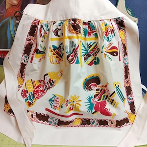 May include: A white apron with a brown, red, and yellow border. The apron has a colorful pattern of Mexican-themed images, including a sombrero, a guitar, and a cactus.