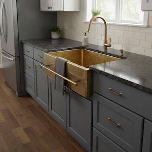 May include: A gold-colored farmhouse sink with a textured surface is installed in a kitchen. The sink is mounted on gray cabinets with gold-colored hardware. A gold faucet and towel bar are also visible.