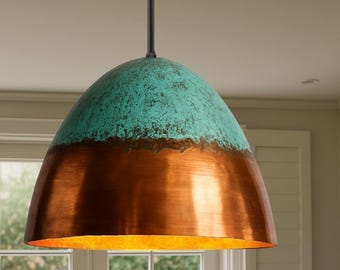 May include: A hanging pendant light with a copper and turquoise finish. The light fixture has a rounded, dome-like shape. The top portion is turquoise, while the bottom is copper. The light is suspended from a black cord.