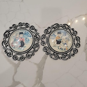May include: Two decorative wall plaques with ornate silver-colored frames. Each plaque features a circular image of Dutch children in traditional clothing. The images are set against a wintery, snowy backdrop.