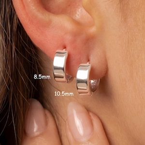 Puede incluir: Dos pendientes de aro de plata pulida con un diseño de banda ancha y lisa. El aro más pequeño está etiquetado como 8,5 mm y el más grande como 10,5 mm, indicando sus diámetros respectivos. Estos pendientes tienen un acabado metálico brillante.