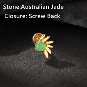 May include: A gold-colored earring with a screw back closure. The earring features a light green Australian jade stone at the center, surrounded by gold-colored leaf-shaped accents. The text on the image reads "Stone: Australian Jade" and "Closure: Screw Back."