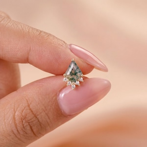 May include: A kite-shaped moss agate stud earring set in gold, featuring a pointed top and a base accented with five small, clear, round-cut white stones arranged in a fan-like pattern along the bottom edge of the gemstone.