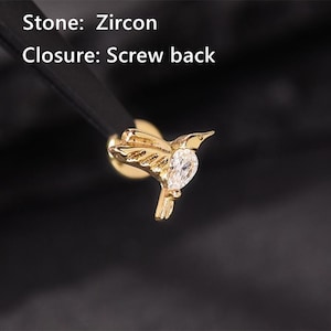 May include: A gold-colored hummingbird earring with a clear, teardrop-shaped zircon stone. The earring has a screw back closure. The text on the image reads "Stone: Zircon" and "Closure: Screw back."