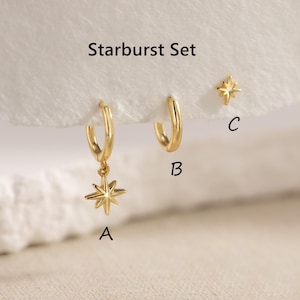 Puede incluir: Un conjunto de pendientes dorados con el texto "Starburst Set". El conjunto incluye un par de pendientes de aro, uno con un dije de estrella, y un par de pendientes de botón en forma de estrella. Los pendientes se muestran sobre una superficie blanca.