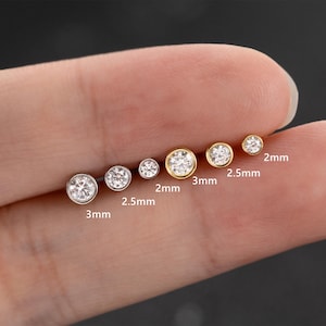 Może przedstawiać: Kolekcja sześciu małych, okrągłych kolczyków sztyftów z przezroczystymi, błyszczącymi kamieniami szlachetnymi. Kolczyki są osadzone w metalu w kolorze złotym i srebrnym. Rozmiary wahają się od 2 mm do 3 mm średnicy.