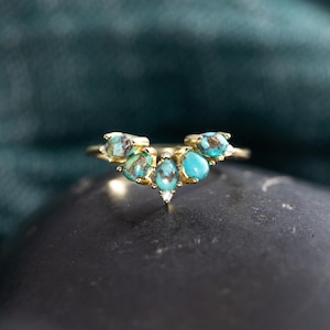 May include: A gold ring featuring a cluster of turquoise stones. The ring has a delicate band and the turquoise stones are teardrop and round shaped. A small diamond is set between the two center turquoise stones.