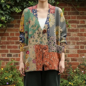 May include: A patterned patchwork cardigan in shades of green, orange, and blue, with two pockets and brown buttons. The person is wearing dark green trousers and brown boots. The cardigan is worn over a white top.
