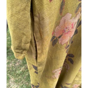 May include: A mustard yellow garment featuring a floral print with soft pink and dark brown petals and leaves. The fabric has a visible woven texture and includes a side seam pocket integrated into the construction of the piece.