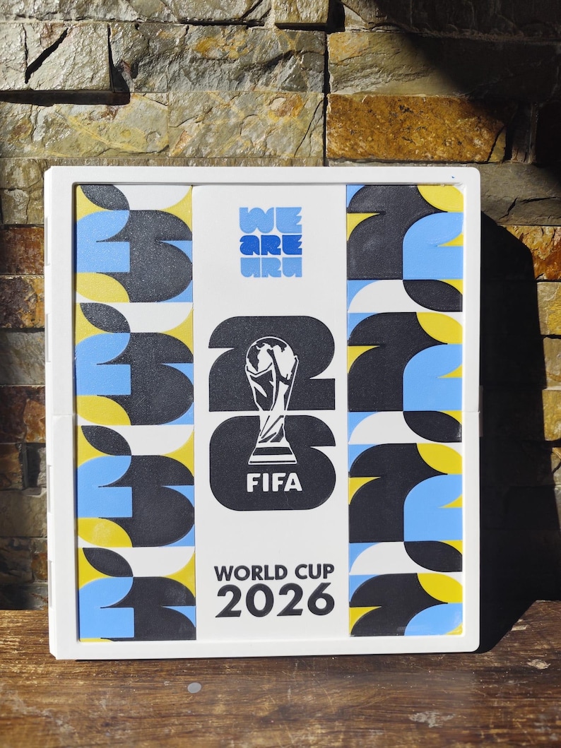 May include: A rectangular white frame containing a graphic display for the FIFA World Cup 2026. The center features the tournament trophy icon, the text WE ARE 26, FIFA, and WORLD CUP 2026. The side panels feature a repeating pattern of black, blue, and yellow.