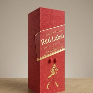 May include: Red rectangular box with the words "Johnnie Walker Red Label" in gold lettering. The box has a textured surface and a gold illustration of a man walking with a cane. Two small red knobs are on the front.