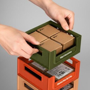 Close-up of hands stacking an orange modular 3D printed box onto a storage tower. Professional studio setting showing the practical use of the StackBox system for organization