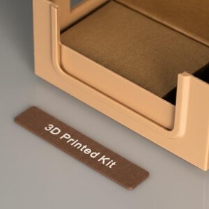 Detailed view of a 3D printed storage bin with a customizable label. The text '3D Printed Kit' is clearly visible on a brown label attached to a beige modular box.