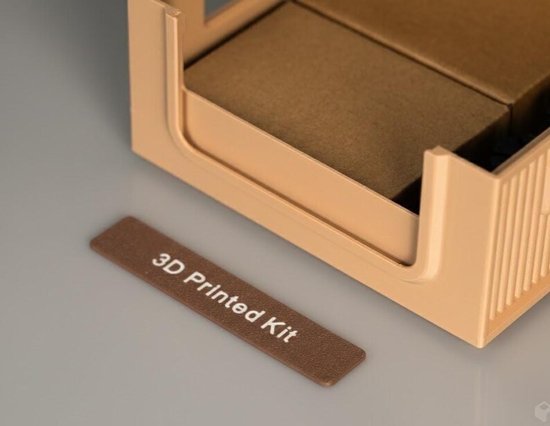 Detailed view of a 3D printed storage bin with a customizable label. The text '3D Printed Kit' is clearly visible on a brown label attached to a beige modular box.