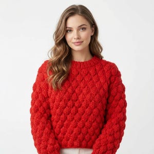 Peut inclure: Un pull rouge vif en tricot avec un col rond. Le pull présente un motif de losanges répétés sur le corps et les manches. Le vêtement est fait d'une matière épaisse et chaude, idéale pour les temps frais.
