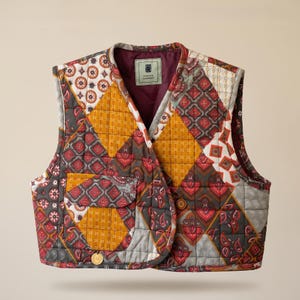 Op de afbeelding: Een gewatteerd vest met een patchworkontwerp van mosterdgeel, donkergrijs en dieprode geometrische en paisley-patronen. Het kledingstuk heeft een V-hals, een voorzak en een label aan de binnenkant van de kraag met de tekst Persian Harmony.
