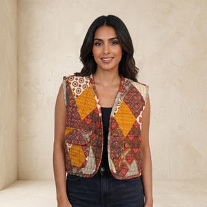 Può includere: Un gilet trapuntato senza maniche con un design patchwork nei toni del marrone, arancione e rosso. Il gilet ha uno scollo a V e due tasche. Il motivo comprende diamanti e rettangoli. Indossato sopra un top nero e jeans blu.