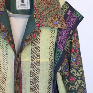 Può includere: Giacca fantasia con base verde e gialla, caratterizzata da ricami intricati e accenti colorati. Il colletto e i polsini presentano disegni dettagliati con piccoli abbellimenti riflettenti. L'etichetta recita "PERSIAN HARMONY".