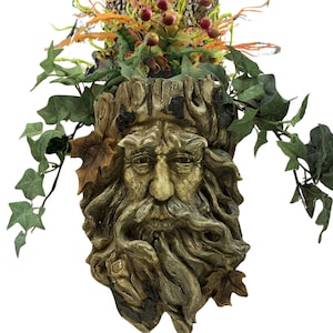 May include: A hanging planter shaped like a weathered tree bark face with a long beard. The planter is filled with green ivy and orange and red berries.