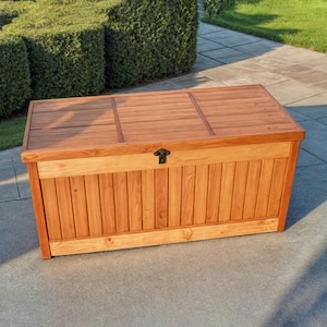 May include: A wooden storage box with a hinged lid and a metal latch. The box is made of natural wood with a light brown finish.