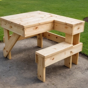 May include: A light-colored, L-shaped wooden table with a matching bench. The table has a rectangular top and a lower bench, all constructed from unfinished wood. The table is supported by angled legs, and the bench is a simple, rectangular design.