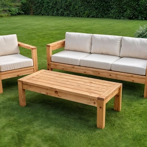 Könnte beinhalten: Gartenmöbel-Set aus Holz mit einem Dreisitzer-Sofa, einem Sessel und einem Couchtisch. Das Set hat cremefarbene Kissen und eine natürliche Holzoberfläche. Die Möbel stehen auf einem grünen Rasen.