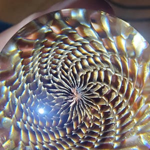 May include: A glass paperweight with a swirling, iridescent pattern in shades of gold, brown, and blue.
