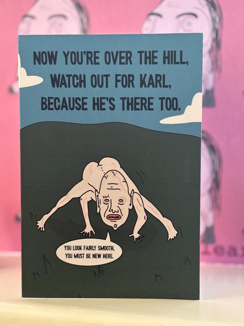 May include: A rectangular greeting card with a blue sky and dark hill background. It features a pale, hairless, four-legged creature labeled Karl. The text reads: NOW YOU'RE OVER THE HILL, WATCH OUT FOR KARL, BECAUSE HE'S THERE TOO. YOU LOOK FAIRLY SMOOTH, YOU MUST BE NEW HERE.