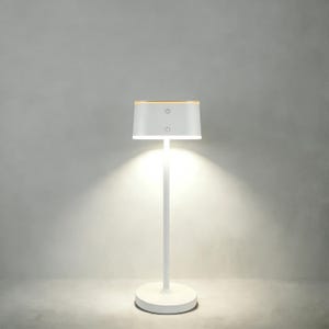 May include: A modern white table lamp with a cylindrical base and a slender stem. The lampshade is rectangular with a wooden top and two power button icons. The lamp emits a warm, bright light.