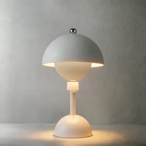 May include: A modern, white table lamp with a unique design. The lamp features a rounded base, a slender stem, and a large, dome-shaped shade. A smaller, spherical element sits below the shade. The lamp is topped with a small, silver-colored knob.