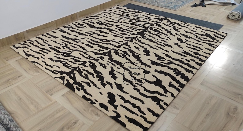 May include: A rectangular area rug featuring a cream-colored base with a repeating black tiger stripe pattern. The rug displays a central black stamp with the text House Of Heritage Rugs. The design covers the entire surface of the floor covering.
