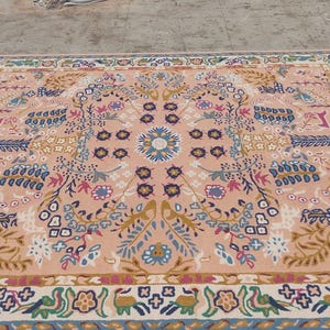 Peut inclure: Un tapis rectangulaire avec un motif floral central dans les tons p&ecirc;che, bleu et or. Le tapis pr&eacute;sente une bordure d&eacute;taill&eacute;e avec des motifs r&eacute;p&eacute;titifs, adapt&eacute; &agrave; la d&eacute;coration int&eacute;rieure. Le tapis porte le texte "House of Heritage Rugs".