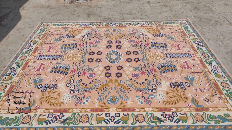 Peut inclure: Un tapis rectangulaire avec un motif floral central dans les tons p&ecirc;che, bleu et or. Le tapis pr&eacute;sente une bordure d&eacute;taill&eacute;e avec des motifs r&eacute;p&eacute;titifs, adapt&eacute; &agrave; la d&eacute;coration int&eacute;rieure. Le tapis porte le texte "House of Heritage Rugs".