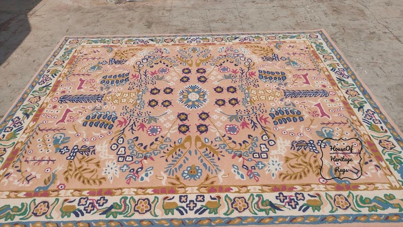 Peut inclure: Tapis rectangulaire avec un motif floral dans les tons p&ecirc;che, bleu, vert et marron. Le tapis pr&eacute;sente un m&eacute;daillon central et une bordure avec des motifs r&eacute;p&eacute;titifs. Le tapis est probablement en laine ou dans une mati&egrave;re similaire.