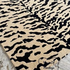 May include: A rectangular area rug featuring a high-contrast black and beige tiger stripe pattern. The rug has a textured pile surface and includes a black decorative border outline in the bottom right corner with the text House Of Heritage Rugs.