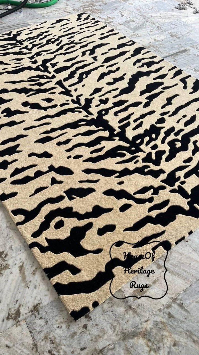 May include: A rectangular area rug featuring a high-contrast black and beige tiger stripe pattern. The rug has a textured pile surface and includes a black decorative border outline in the bottom right corner with the text House Of Heritage Rugs.