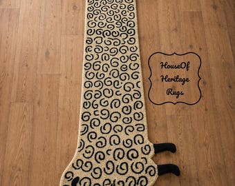 May include: A long, narrow rug shaped like a sheep with a cream-colored body featuring a black spiral pattern. The sheep has a solid black head and four black legs. The text HouseOf Heritage Rugs is printed in black within a decorative border.