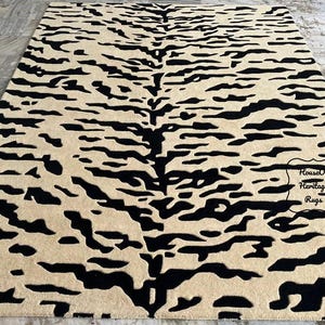 May include: A rectangular area rug featuring a high-contrast tiger stripe pattern in black and beige. The design consists of irregular, horizontal black stripes across a solid beige background. A small label reads House Of Heritage Rugs.