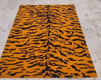 May include: A large orange and black tiger stripe rug. The rug has a black border and is made of a soft, plush material. The rug is perfect for adding a touch of style and comfort to any room.