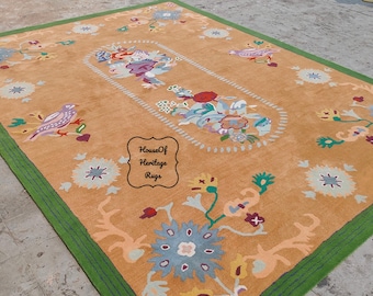 May include: A large, rectangular rug with a tan background and a green border. The rug features a floral design with birds and flowers in shades of blue, green, pink, and yellow. The text "House Of Heritage Rugs" is printed in the center of the rug.