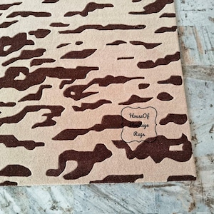 May include: A rectangular area rug featuring a high-contrast abstract pattern of dark brown organic shapes set against a light beige background. The rug includes a black outlined logo with the text House Of Heritage Rugs printed in the lower right.