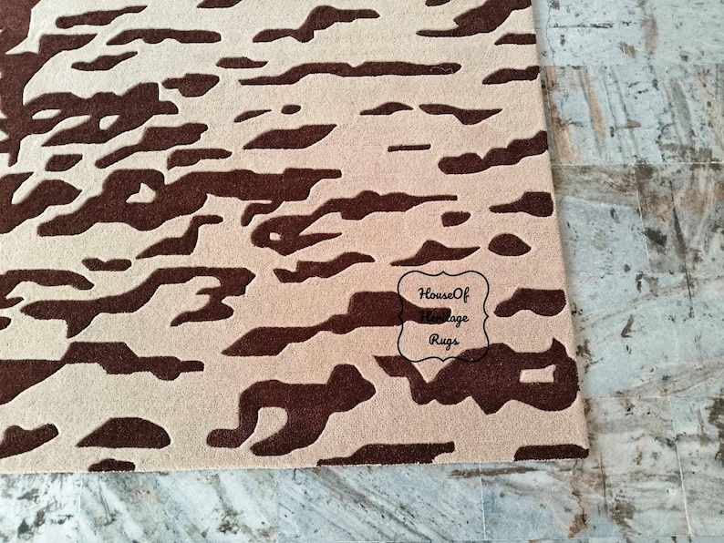 May include: A rectangular area rug featuring a high-contrast abstract pattern of dark brown organic shapes set against a light beige background. The rug includes a black outlined logo with the text House Of Heritage Rugs printed in the lower right.