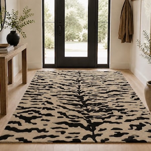 May include: A rectangular area rug featuring a high-contrast tiger stripe pattern in black and beige. The design consists of irregular, horizontal black markings distributed across a solid beige background, covering the entire surface of the rug.
