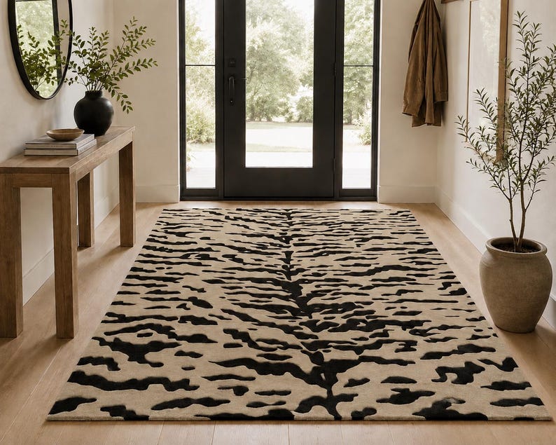 May include: A rectangular area rug featuring a high-contrast tiger stripe pattern in black and beige. The design consists of irregular, horizontal black markings distributed across a solid beige background, covering the entire surface of the rug.
